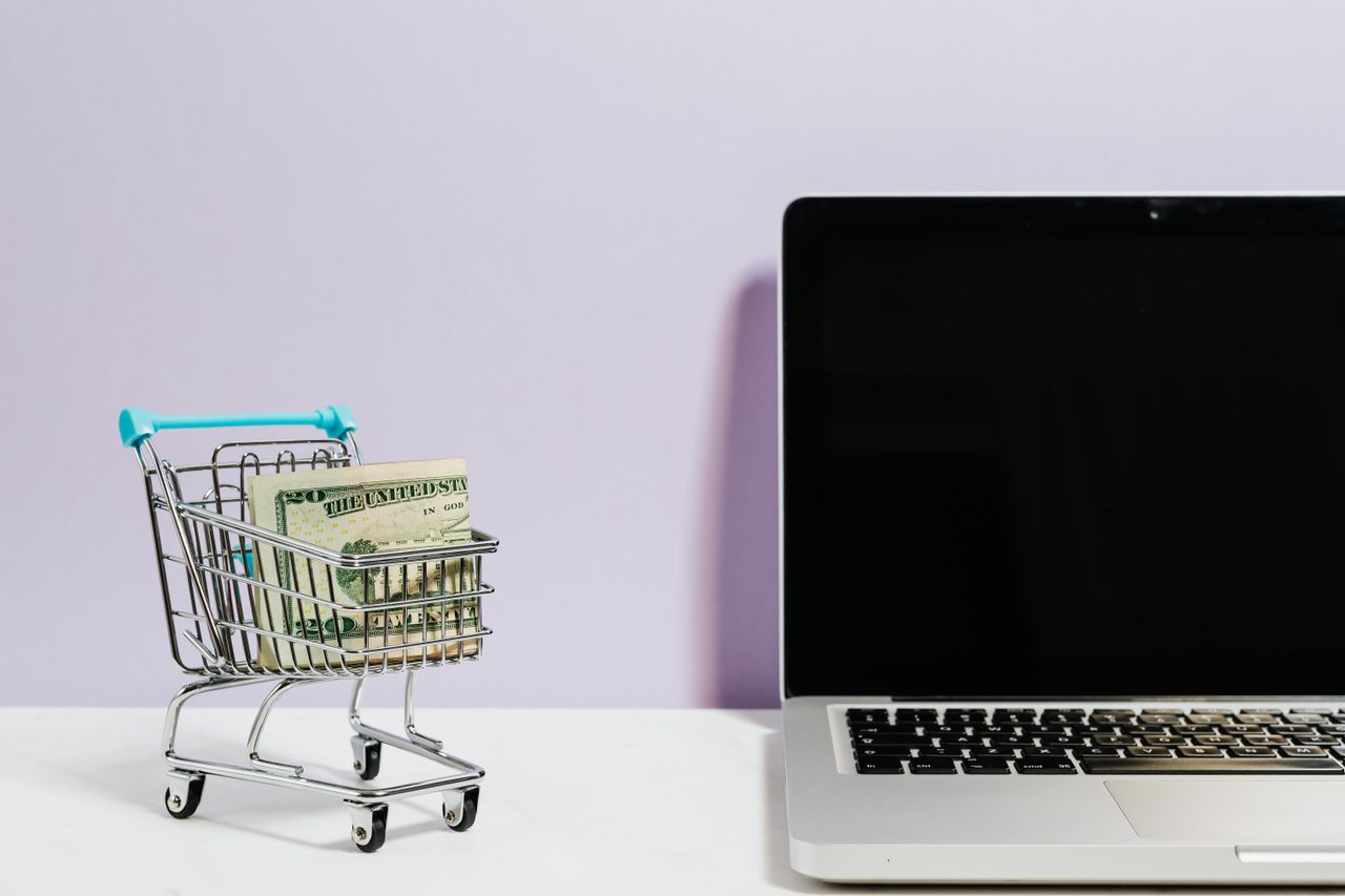 gallery-1 Shopping cart with money next to a laptop symbolizing online shopping and e-commerce.